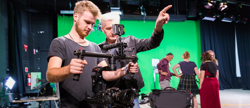 A student holding a camera gimbal, with a green screen in the background