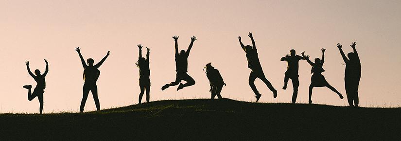 Group of people silhouetted jumping on a hilltop at dusk
