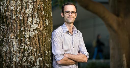 Associate Professor Harry Hobbs leans against a tree with his arms crossed.