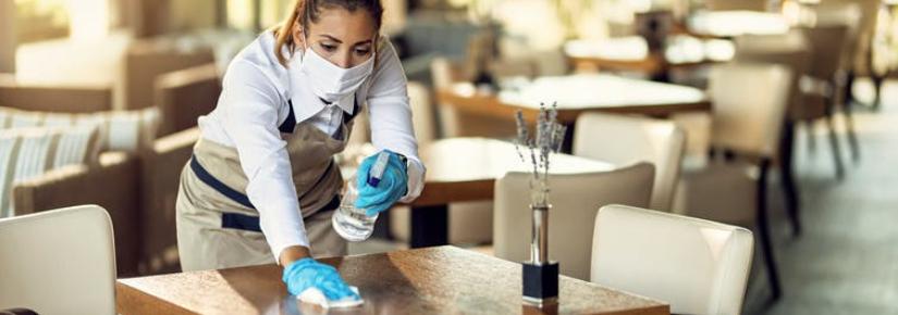 a waitress in a mask and gloves cleans a table