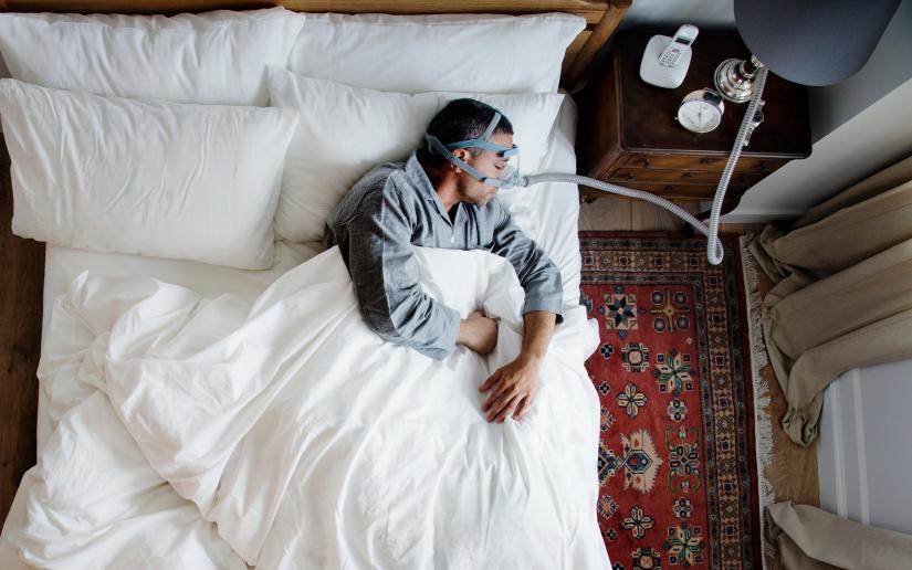 Stock picture of a sleeping man in bed using a CPAP machine 