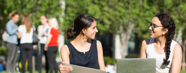 Two female students with laptops on the UTS Alumni green