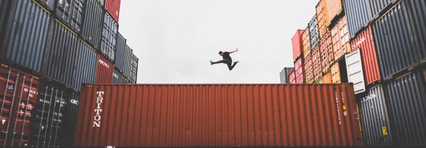 Image of a person jumping on top of a shipping container that is in between two large stacks of shipping containers