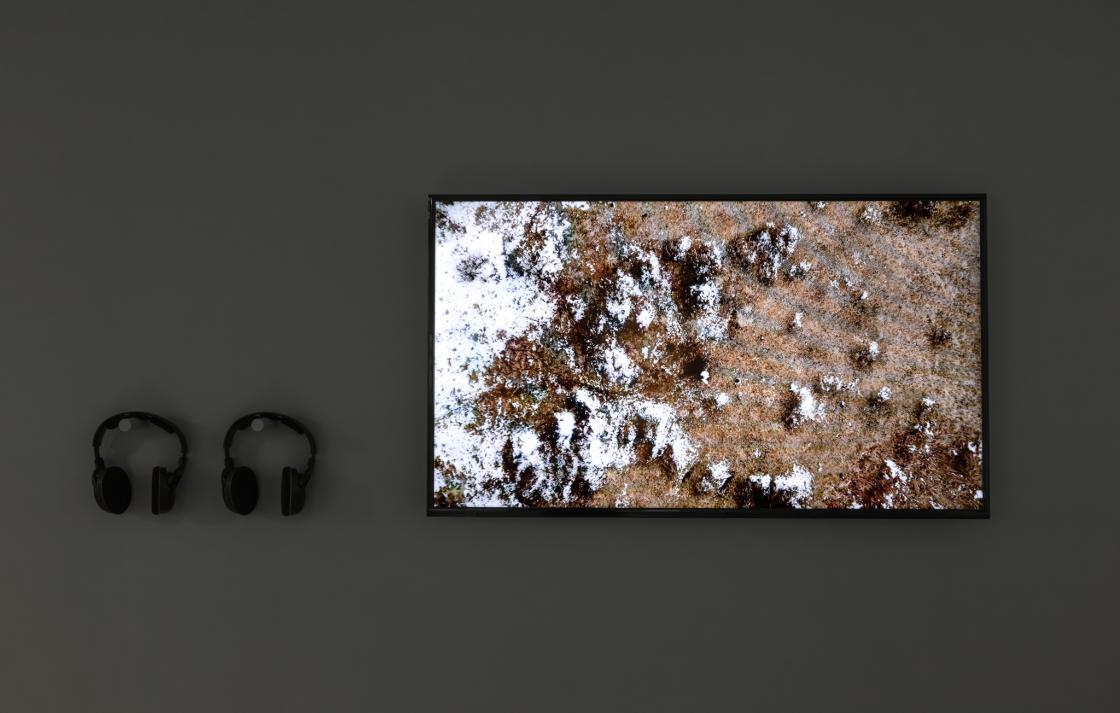 A tv monitor on a wall with two pairs of headphones. The tv shows an aerial view of a rocky landscape