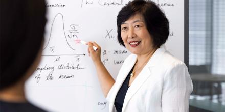 Distinguished Professor Jie Lu wearing a white jacket. She is discussing machine learning theory with a colleague while standing in front of a whiteboard with her pen poised