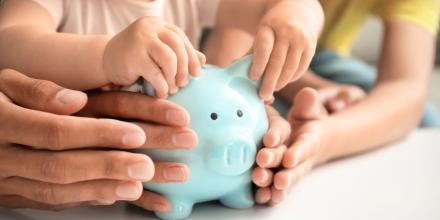 Small child and parents hands holding a piggy bank