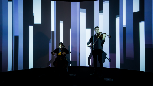 Two musicians playing in front of an artwork projection