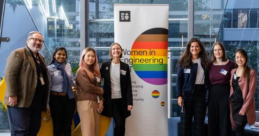 Women around the banner of Women in Engineering and IT posing in front of the banner