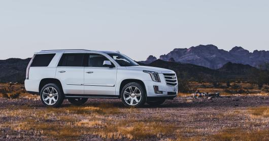 a white SUV sits on a dirt path with mountains in the background.
