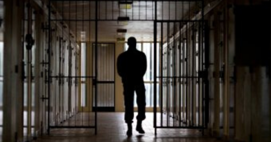 Silhouette of a man walking through a prison corridor.