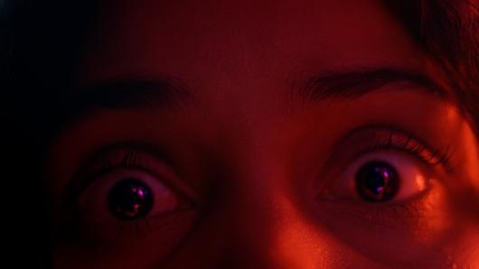 Close-up shot of a woman's eyes widened in panic with a red hue