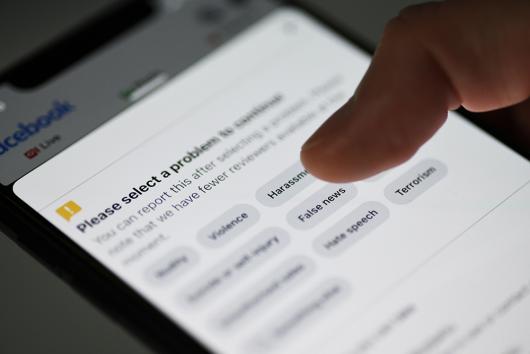 Stock picture of a detail of Facebook App section false news report, on a smartphone.