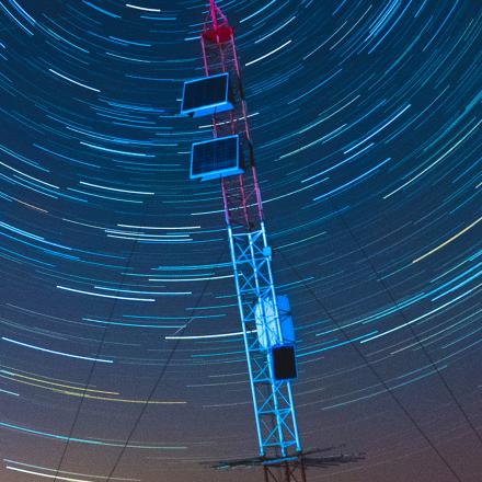 An antenna at dusk with dramatic star trails in the sky above