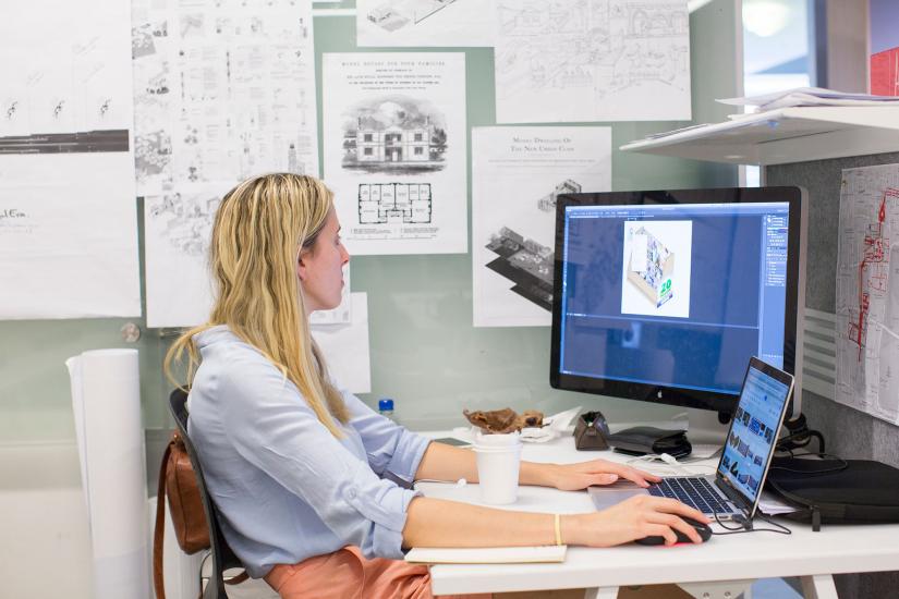 UTS student sitting at a computer with surrounded by architectural drawings