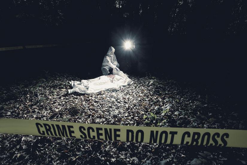 Beyond the yellow tape that reads crime scene do not cross is a crime scene investigator looking at body
