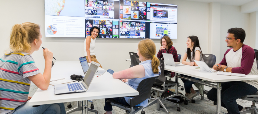 Students sitting in a classroom with news displayed on screens behind
