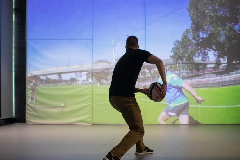 Man about to pass a football in front of a projection screen 