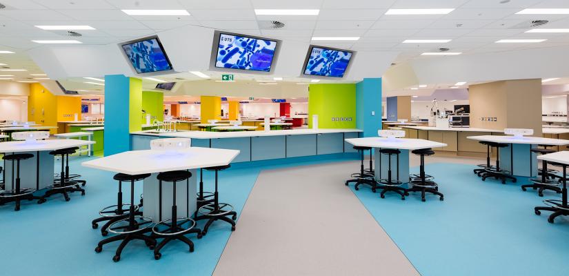 A colourful lab environment with blue, yellow and green walls and floors, white benches, and multiple large screens.