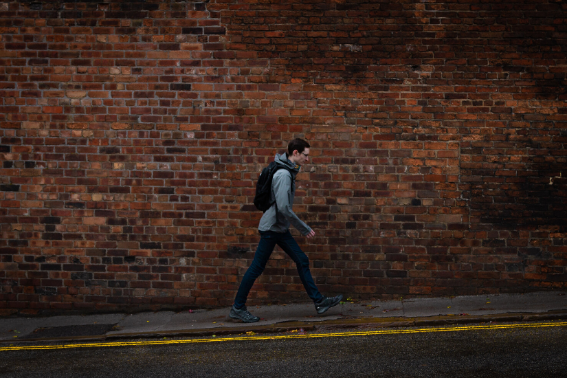 Lonely man with backpack walking on street with brick background.