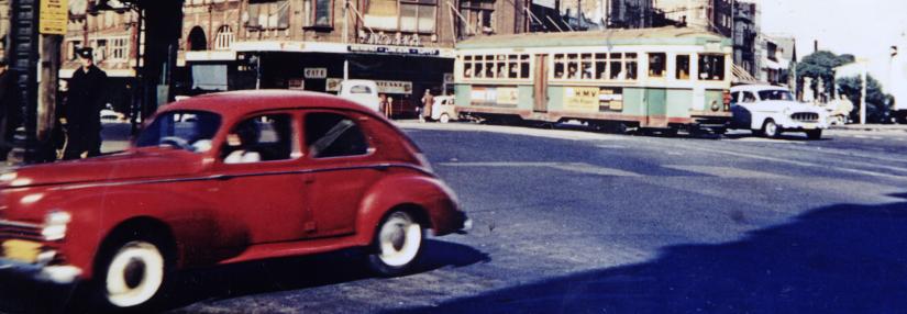 1950s Darlinghurst traffic. Red car in foreground, tram in background.