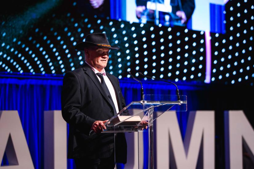 Jack Beetson standing at lectern at UTS Alumni Awards. He is wearing a black suit and tie, and wide brimmed black hat.