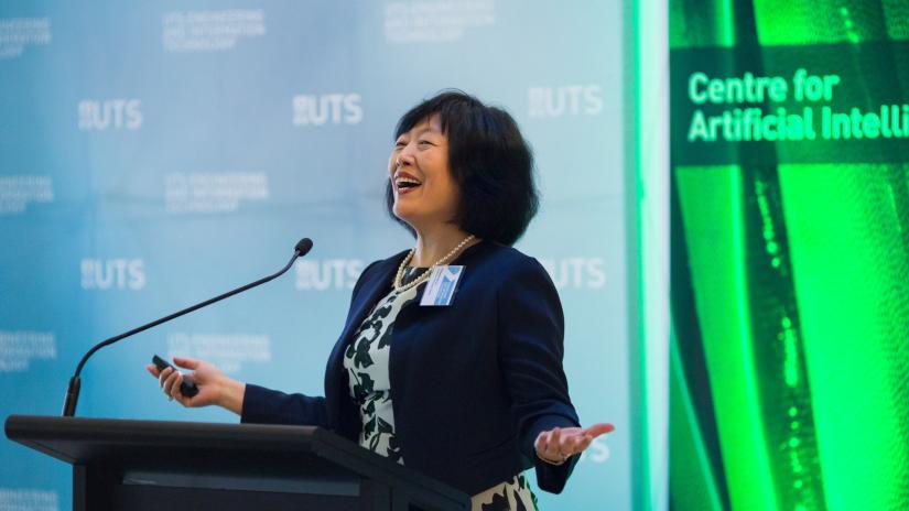 AAII's Distinguished Professor Jie Lu delivering a speech at a podium with a smile and her arms outstretched. UTS and CAI Banner in the background. The image was taken at the launch of CAI, which was re-named AAII in 2020. 