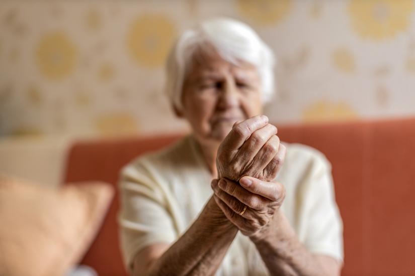 An older person holds one hand to thier wrist, face expressing pain.