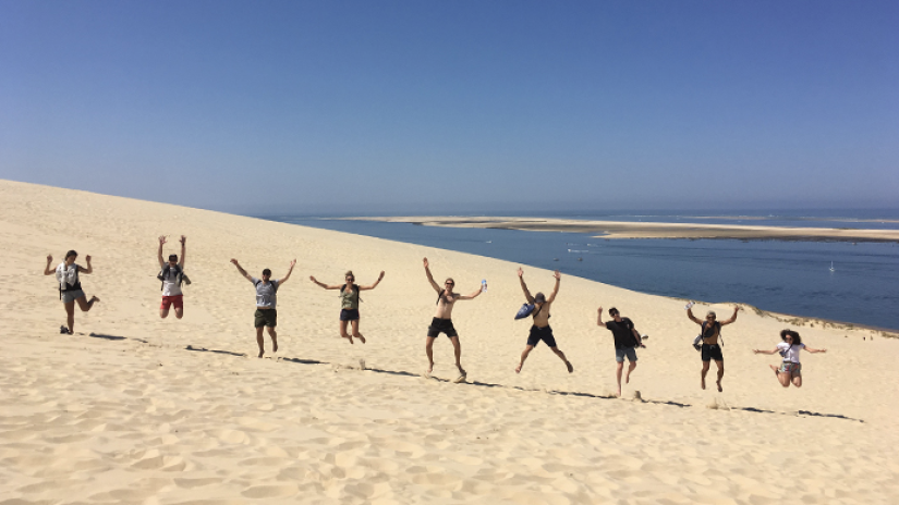 A group of people standing on a sand dune with a body of water in the background