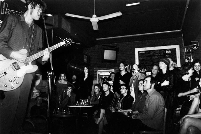 Black and white photo of musician with guitar and crowd watching 