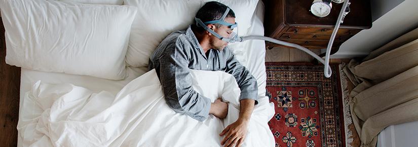 Stock picture of a sleeping man in bed using a CPAP machine 