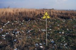 Yellow triangle with biohazard symbol warning on abandoned territory with trash. Garbage waste field with biological hazard sign. Concept of ecology, environmental pollution and danger.