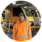 Young man in hi-vis workwear stands in front of parked trains.