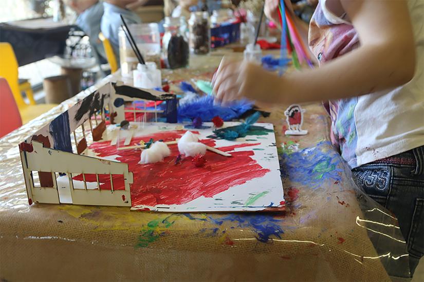A child works on a model of a classroom with paint and craft materials