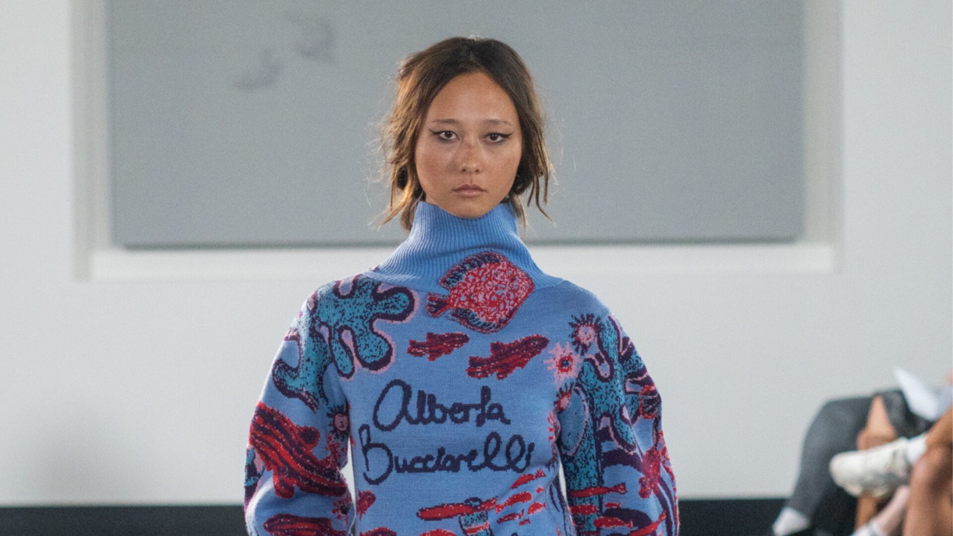 Model on the runway wearing a light blue knitted dress featuring aquatic animals and plants