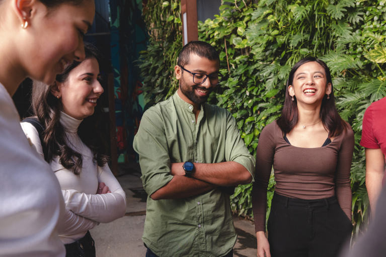 Group of smiling male and female students standing outside UTS Engineering and IT building with a green plant wall behind them.