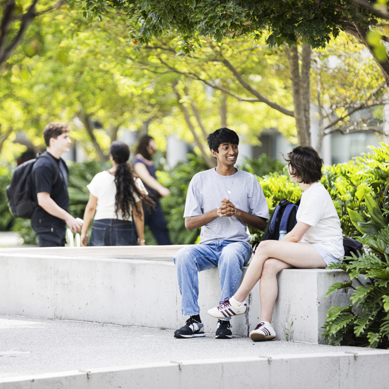 Two students sitting on a concrete bench outside UTS alumni green, engaged in conversation and enjoying the outdoor scenery.