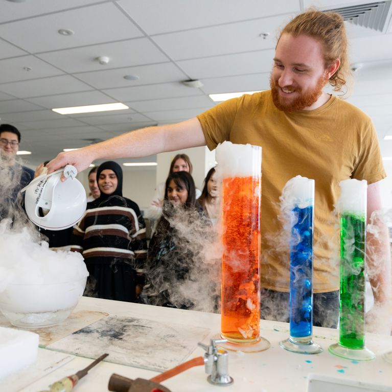 Male student using beakers with coloured liquid in a science class.