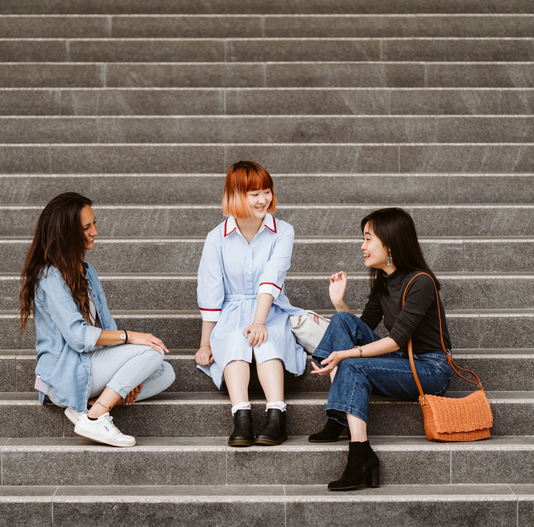 Three UTS international students sitting on stairs chatting.