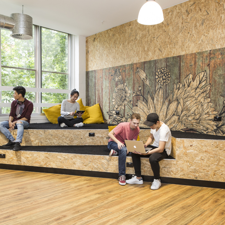 Students seated on wooden benches in an office setting, engaged in discussion and collaboration.