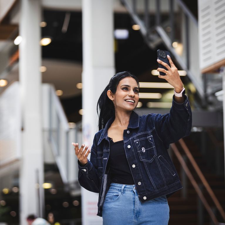 Female student on campus holding up a phone and filming herself speaking.