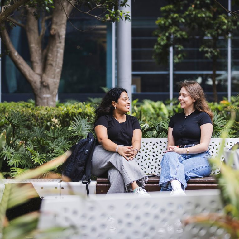 Two female students with laptops on the UTS Alumni green