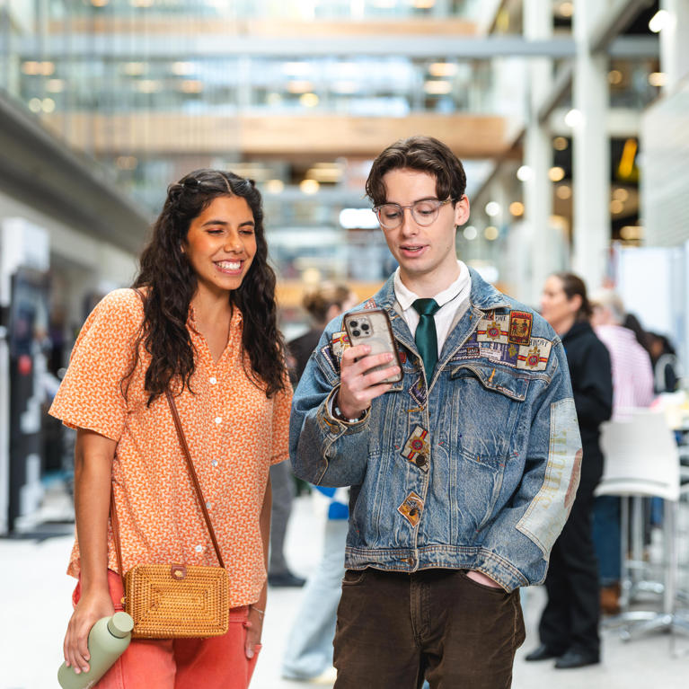 Two prospective students viewing information on a smartphone while exploring the UTS campus during Open Day.