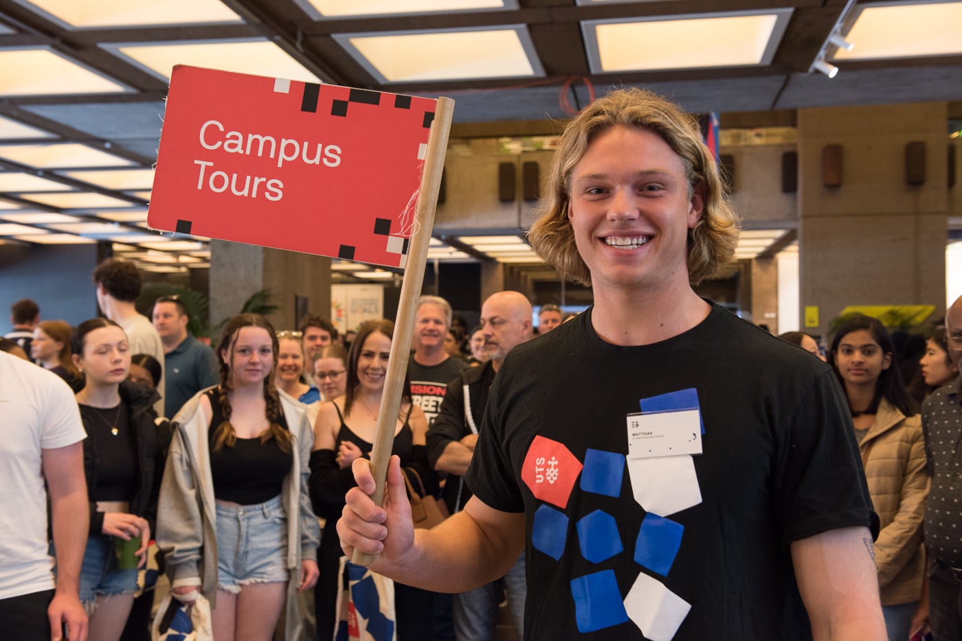 UTS student ambassador displays a sign that says "Campus Tours," inviting people to join guided tours of UTS campus.