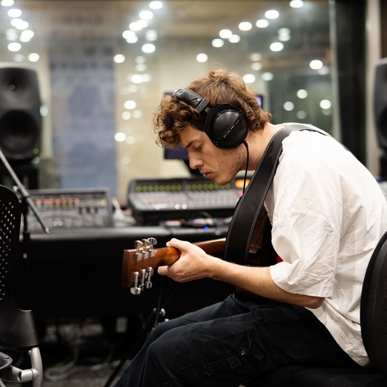 Student in sound room with guitar.
