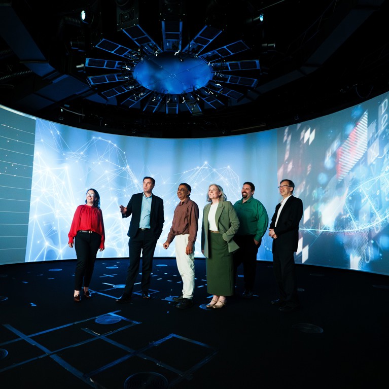 Six members of the UTS Rapido leadership team standing in the UTS Data Centre in front of a giant screen showcasing data driven graphics.