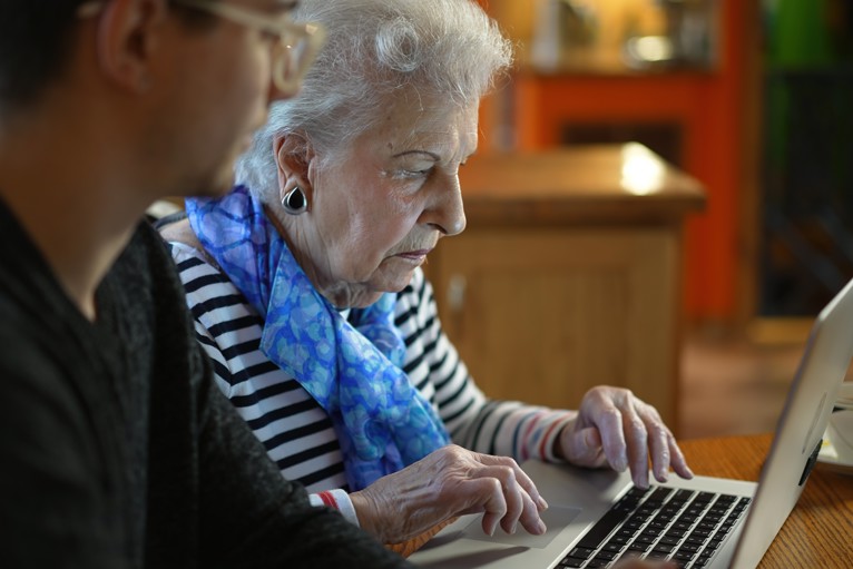 Closeup of elderly senior woman learning to use a laptop computer from a younger person.