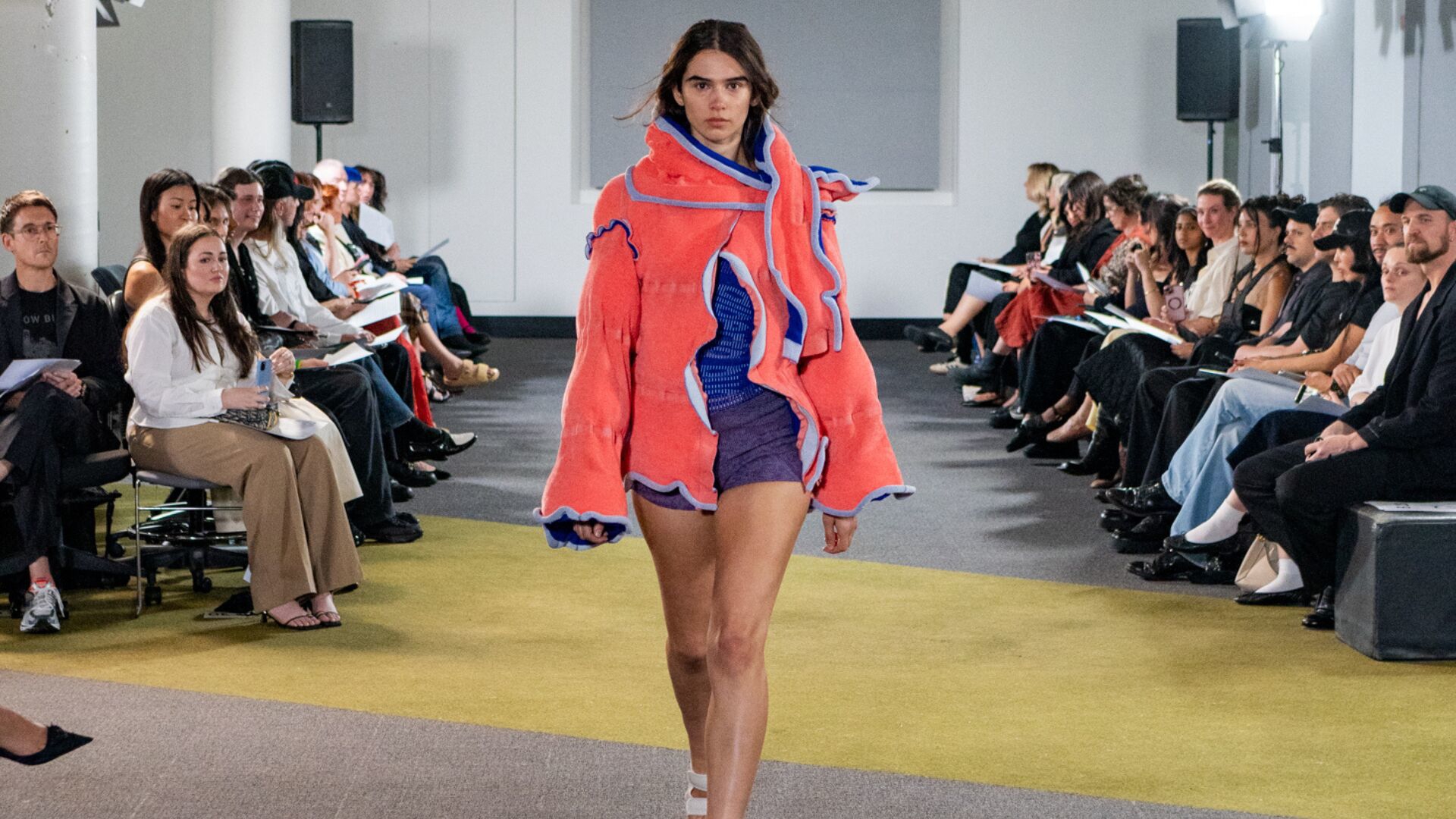 Model on the runway wearing a blue knitted dress with an orange jacket