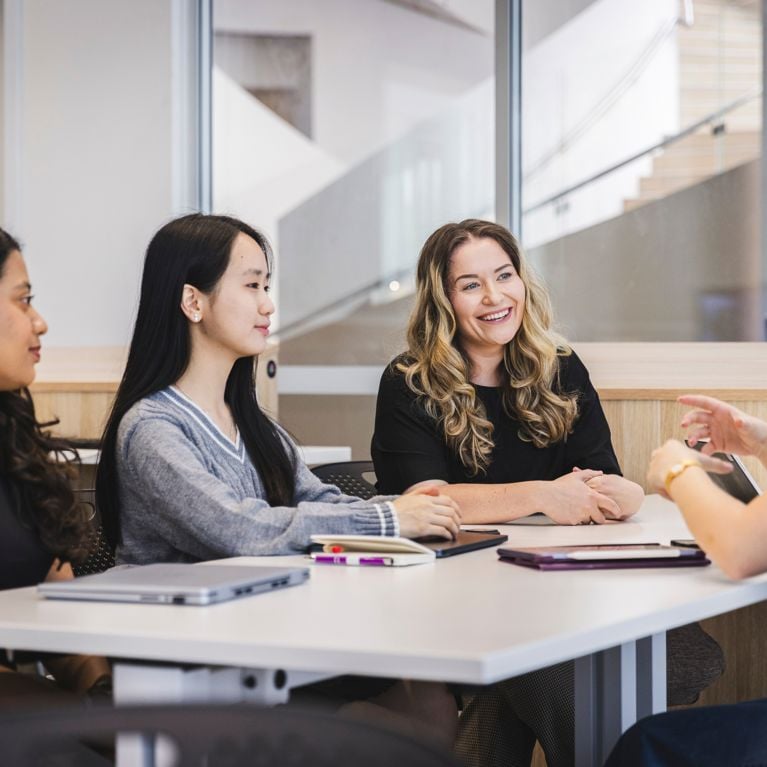Group of students sitting with an academic in classroom setting.