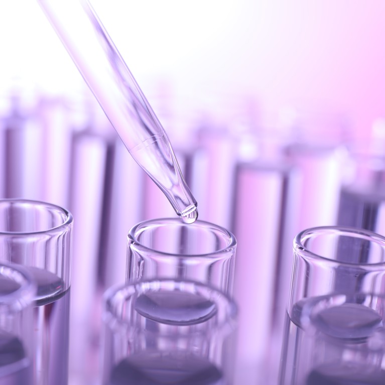 Dripping liquid from pipette into test tube on violet background, closeup
By New Africa