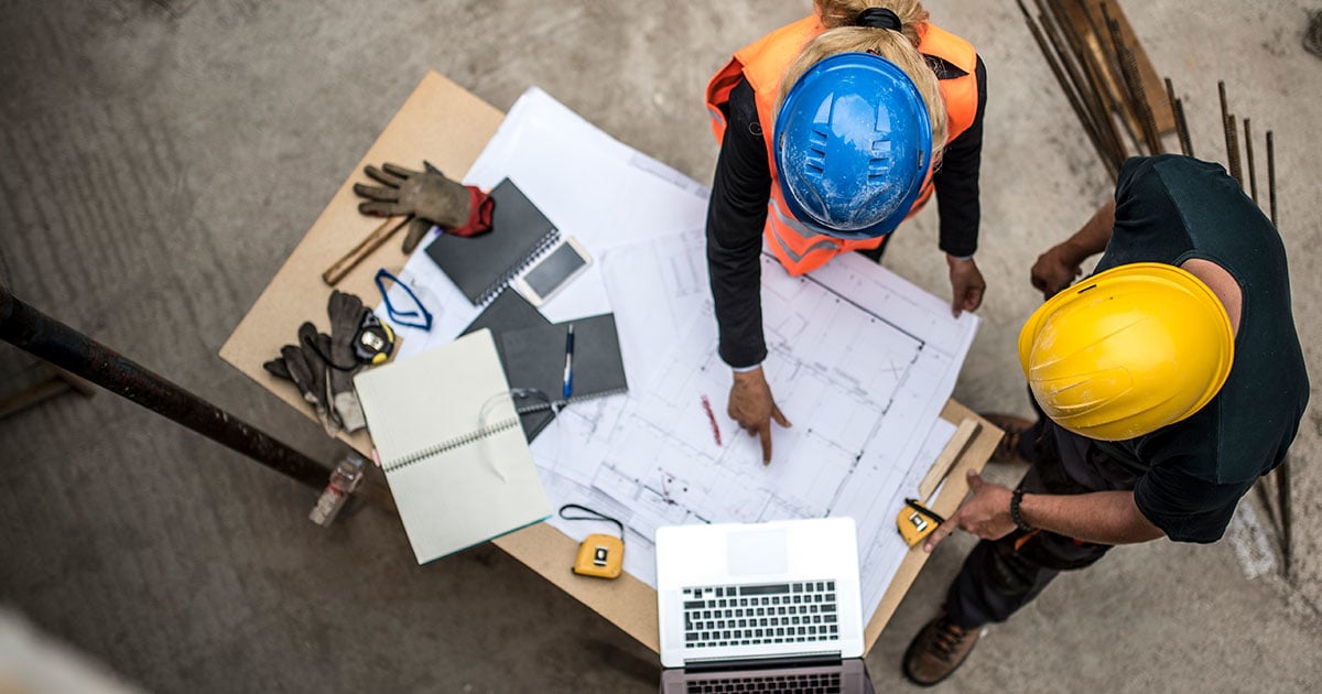 Overhead shot of two people in hard hats looking over a blueprint